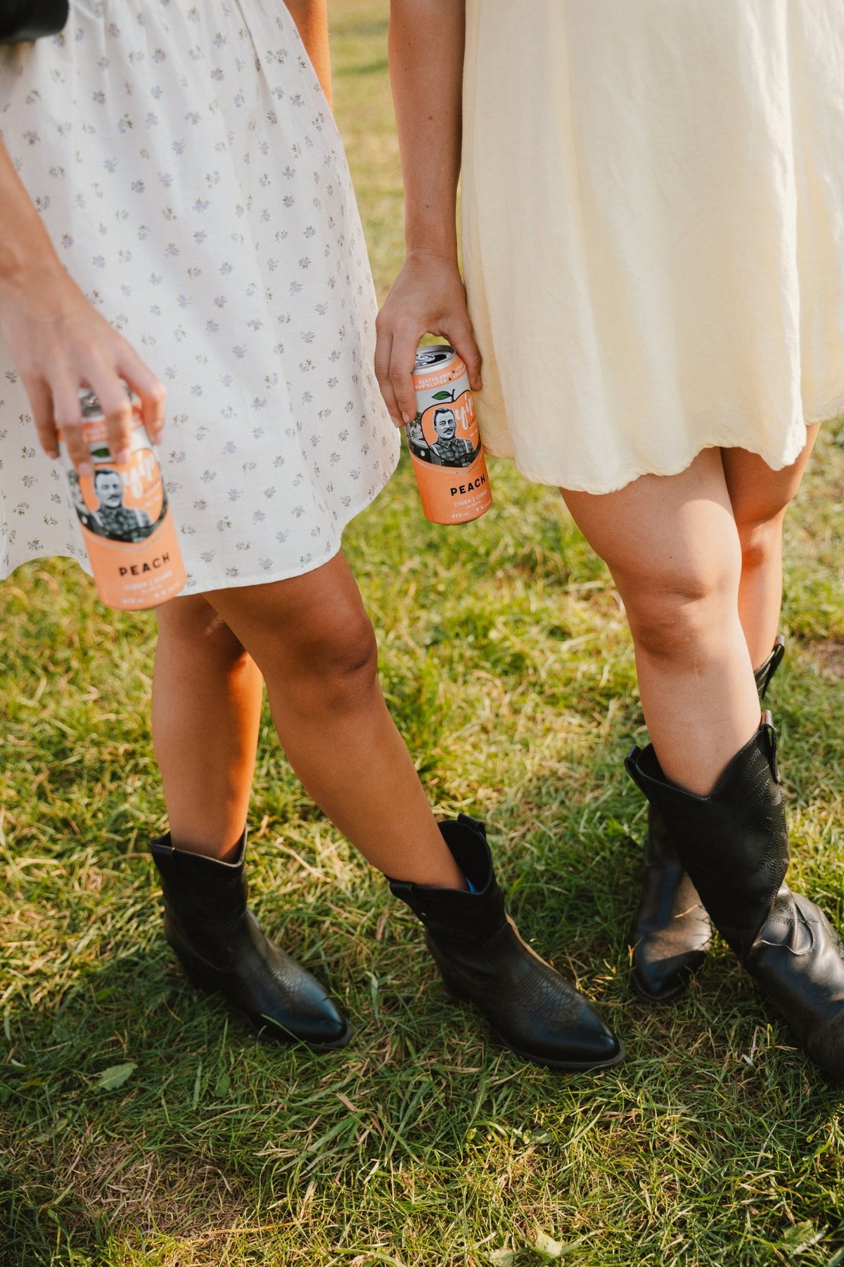 Cans of Yip Peach held low beside cowboy boots on the grass