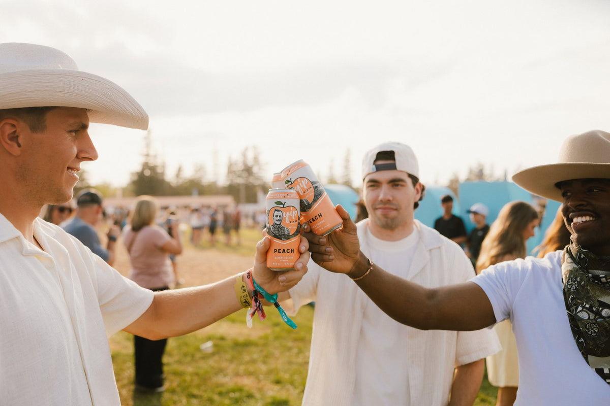 Three friends in cowboy hats clinking cans of Yip Peach