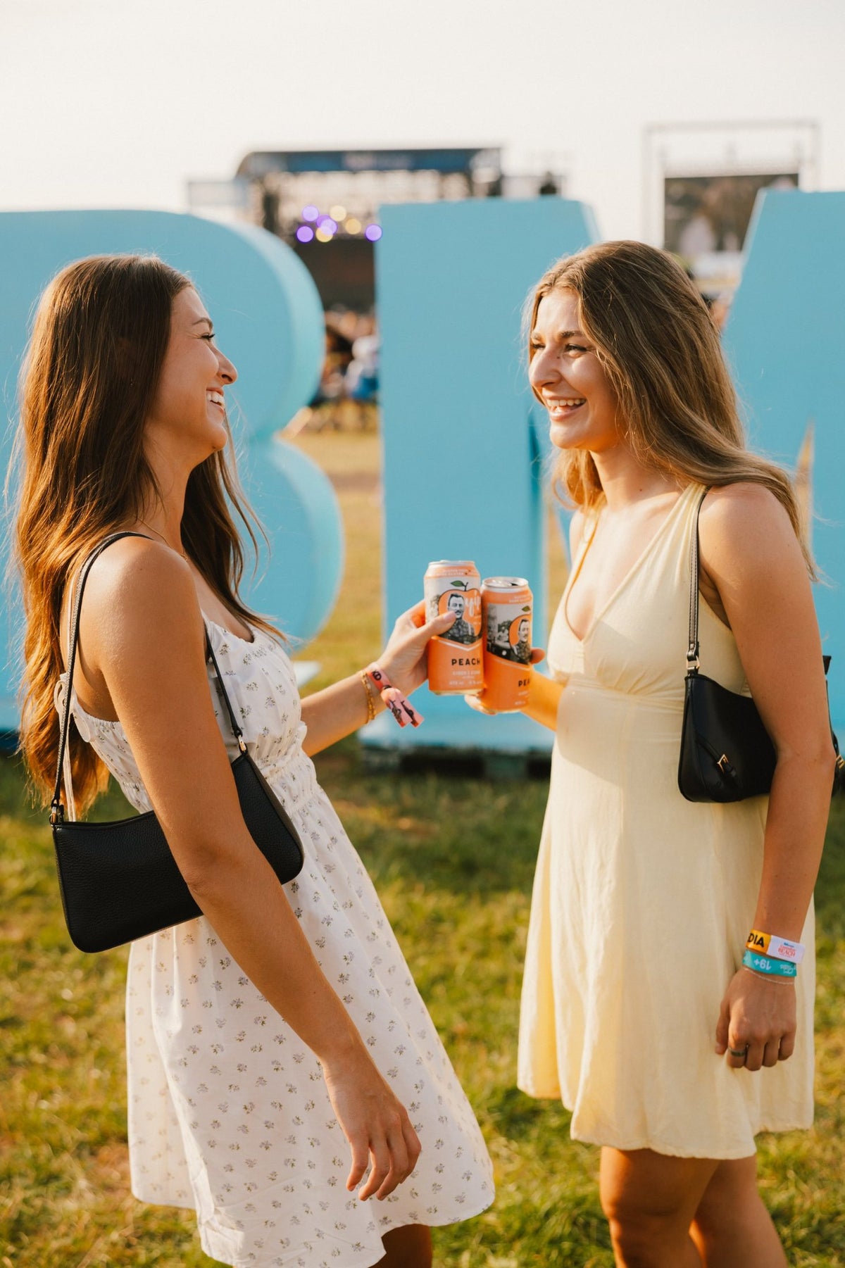 Two friends laughing and clinking cans of Yip Peach in front of the CBMF letters