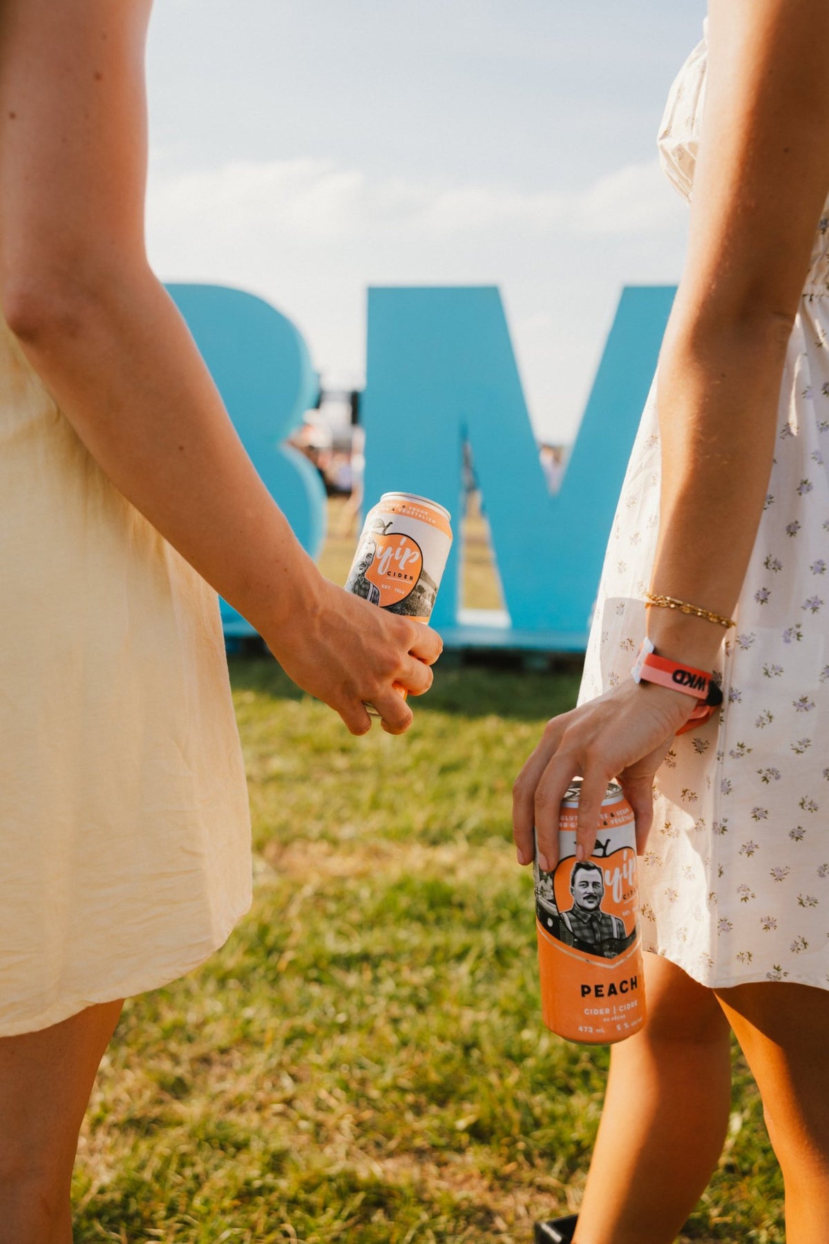 Two cans of Yip Peach held in front of the blue CBMF letters