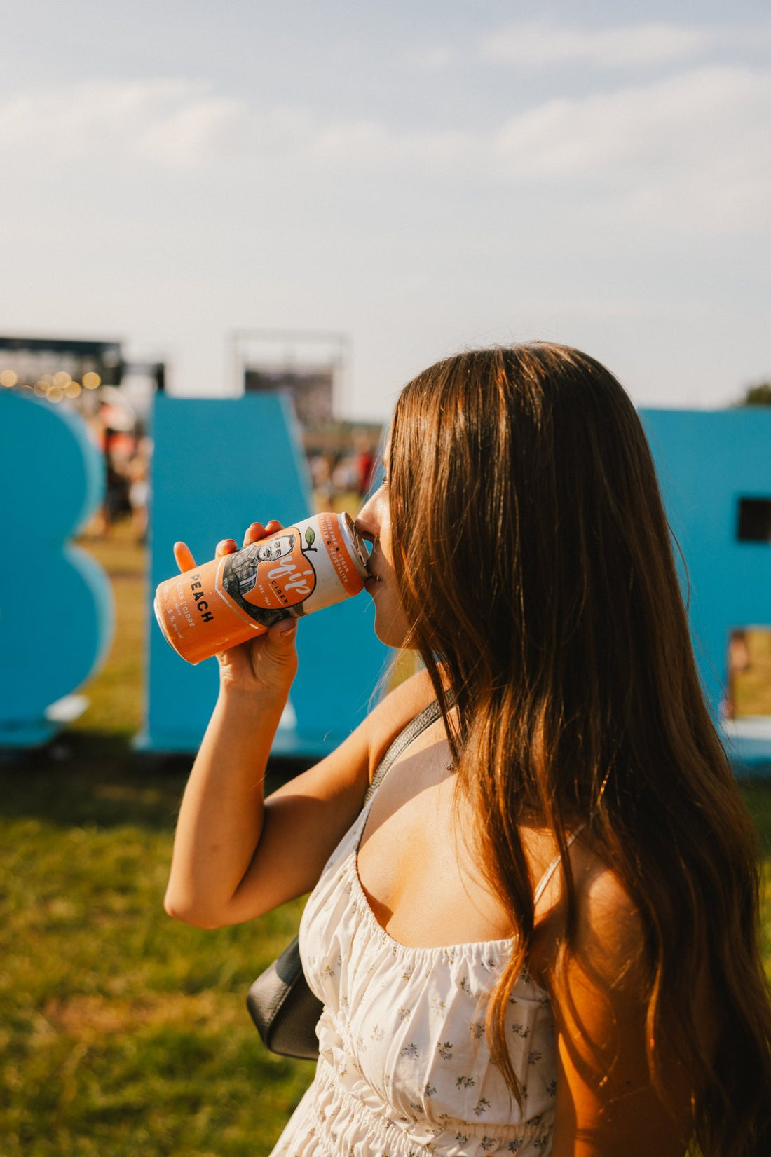 A festival-goer sipping Yip Peach in front of the blue CBMF letters